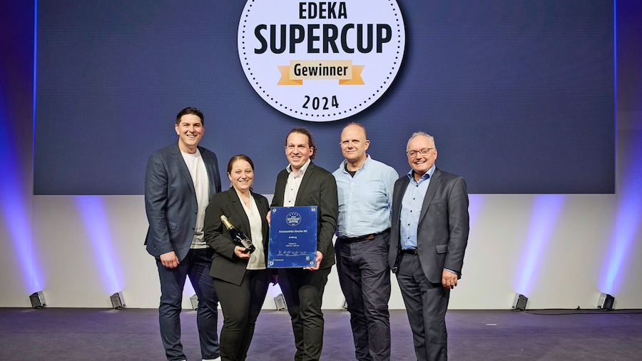 Vier Männer und eine Frau zeigen ihre Sieger-Urkunde auf einer Bühne vor einer Leinwand mit dem Text EDEKA Supercup Gewinner.