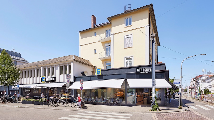 Außenaufnahme des EDEKA-Markts Strecker mitsamt Bäckerei an einer Kreuzung mit Zebrastreifen.