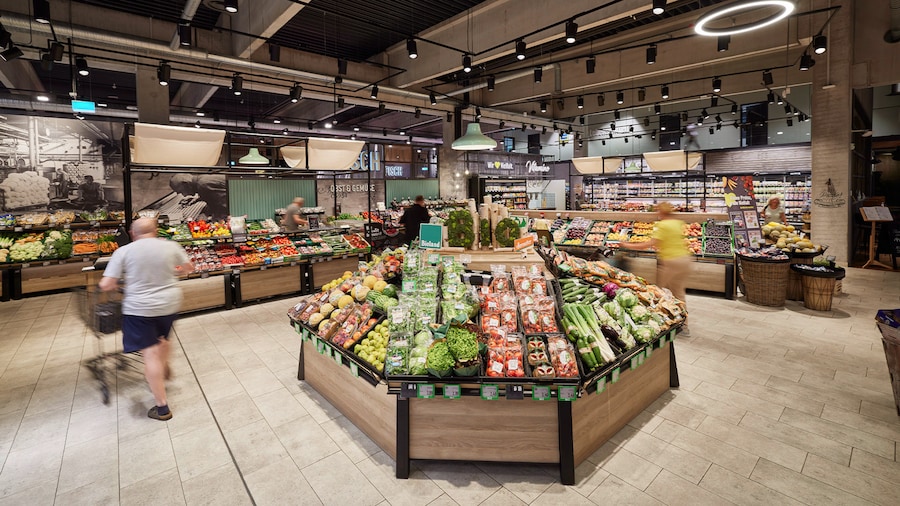 Kunden laufen durch eine weitläufige Obst- und Gemüseabteilung mit vielen Auslageflächen.