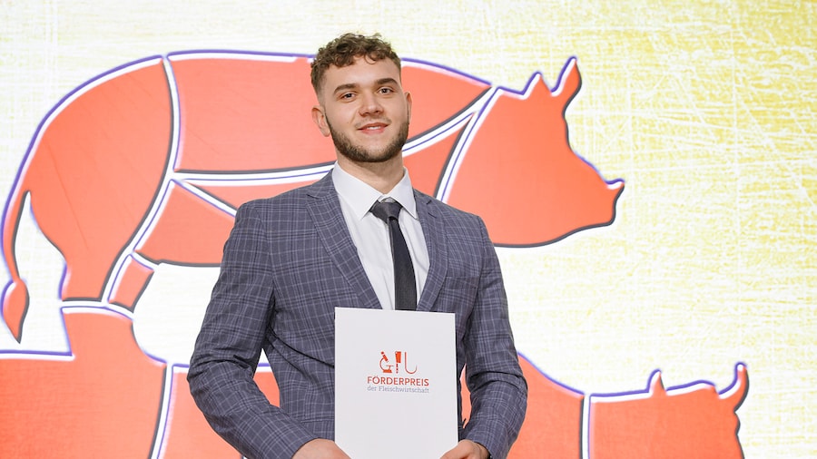 Preisträger posiert mit Zertifikat vor einer Wand mit Fleischmotiv beim Förderpreis.