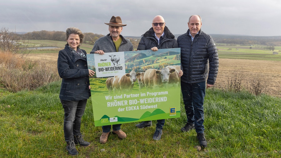 Vier Personen stehen auf einem Feld und präsentieren ein Schild mit dem Hinweis auf ihre Partnerschaft.