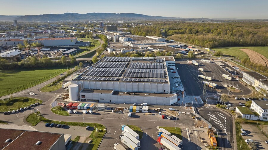 Luftaufnahme der Baustelle eines modernen Tiefkühllager-Gebäudes mit Photovoltaik-Modulen auf dem Dach und Lkw-Parkplätzen.