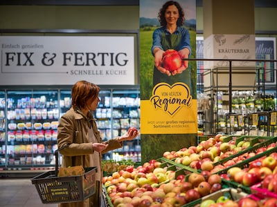 Eine Kundin begutachtet einen Apfel in der Obst- und Gemüseabteilung eines Supermarkts.