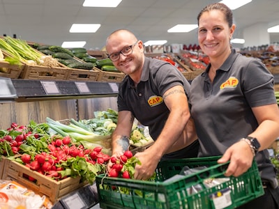 Zwei lächelnde CAP-Markt-Mitarbeitende räumen Radieschen in der Obst- und Gemüseabteilung ein. 