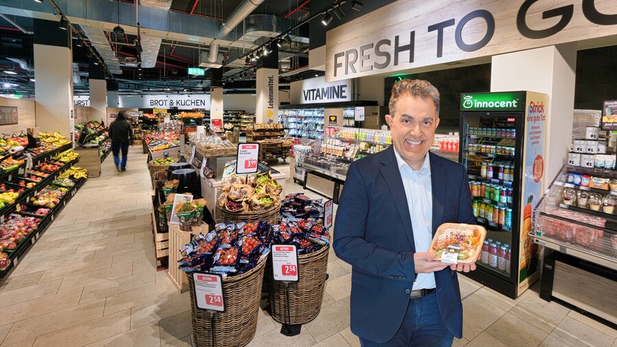 EDEKA-Kaufmann Jafar Graf steht im Inneren seines Marktes und präsentiert ein abgepacktes Convenience-Produkt. 