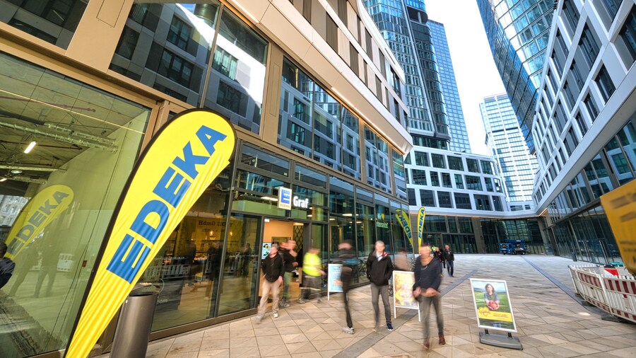 Äußerer Eingangsbereich eines EDEKA-Markts in einer Fußgänger-Passage zwischen hohen Bürogebäuden.