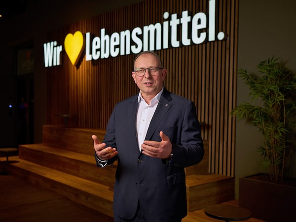 Vorstandssprecher Rainer Huber spricht und gestikuliert vor einer Wand mit dem Marken-Claim 