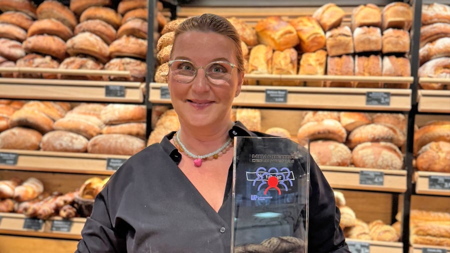 Nina Krämer mit Glastrophäe vor den vollen Regalen einer Marktbäckerei. 