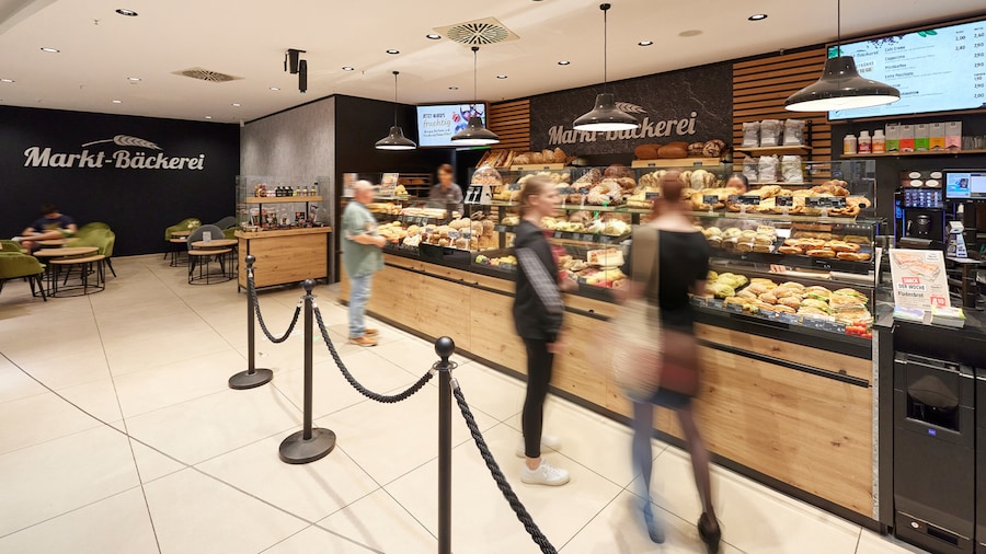 Kunden vor der Theke einer Marktbäckerei mit Sitzplätzen. 