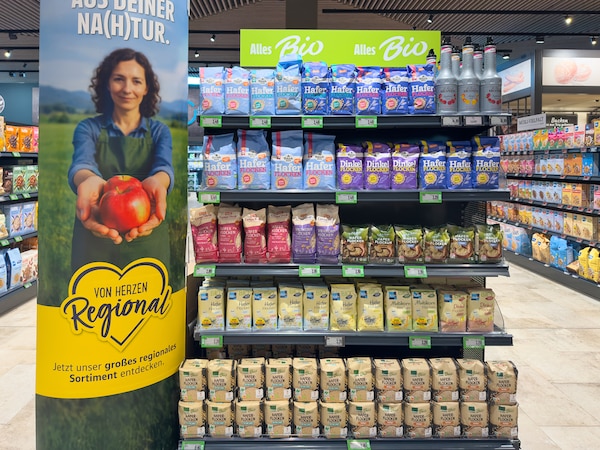 Supermarktregal voller abgepackter Bio-Produkte neben einem Aufsteller, der regonale Lebensmittel bewirbt. 