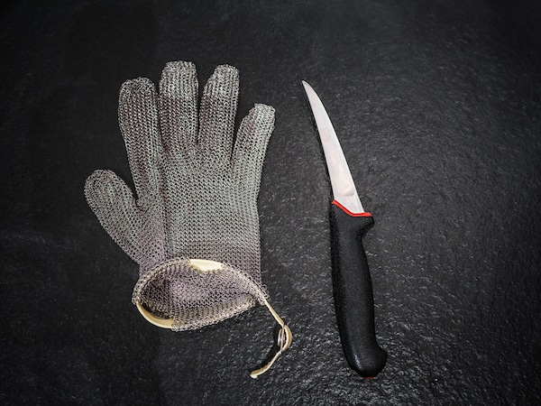 Ein Kettenhandschuh neben einem scharfen Messer auf einer schwarzen Arbeitsfläche. 