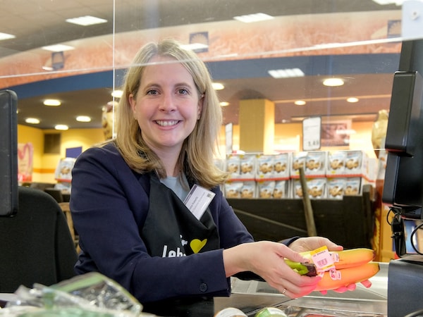 Die Bundestagsabgeordnete Verena Hubertz sitzt lächelnd an der Supermarkt-Kasse und zieht Waren übers den Scanbereich. 