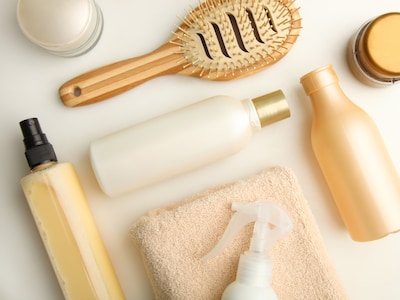 Cremefarbene Tiegel, Spühflasche, Handtuch und Haarbürste liegen auf einem cremefarbenen Tisch.