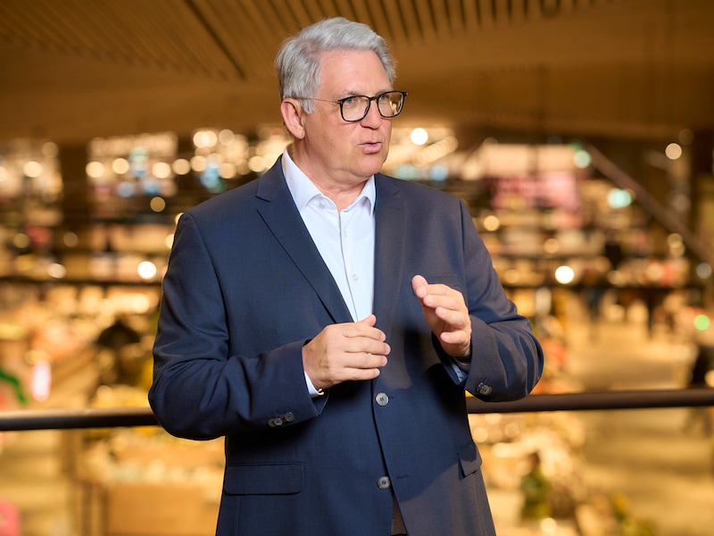 Portrait Uwe Kohler. Mann mit grauem Haar, trägt Brille weißes Hemd und Jackett. Er spricht uns gestikuliert mit den Händen. 