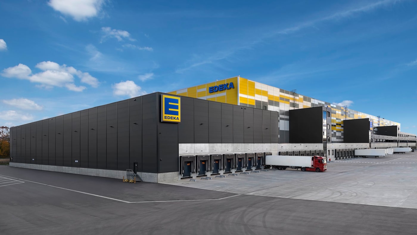 Aussenansicht Zentrallager Rastatt: Vor den zahlreichen Warenausgangstoren steht ein LKKW sowie eingige Anhänger. 