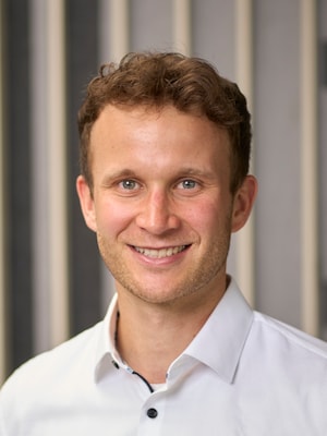 Portrait von Lucas Bürkle. Er lächelt und trägt ein weißes Hemd. 
